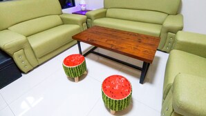 A living room with a green sofa set, a wooden coffee table, and two small watermelon stools. - Bam House B&B (Tainan)