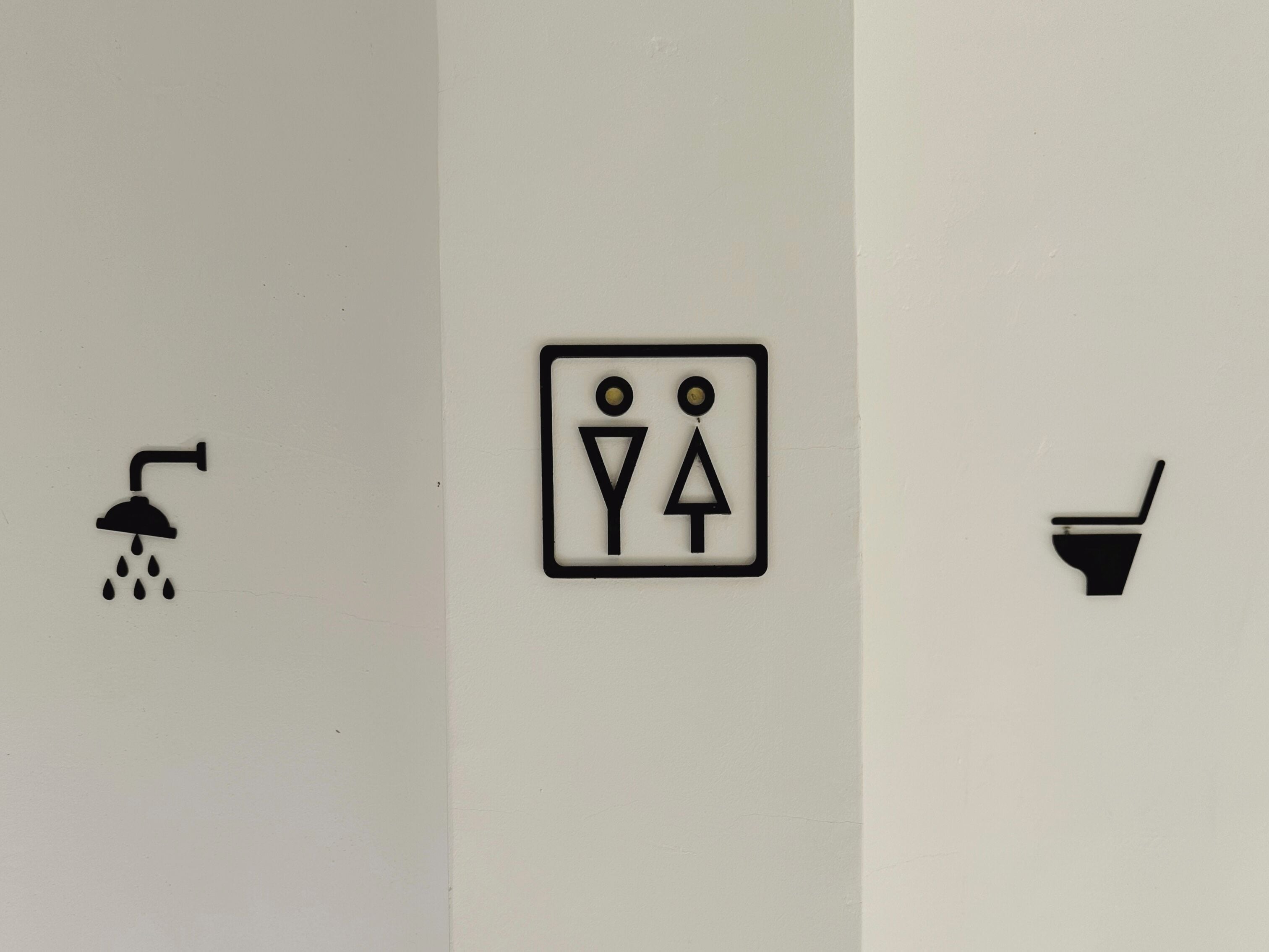 A restroom sign with a shower, a toilet, and a urinal symbol.
