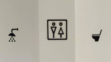 A restroom sign with a shower, a toilet, and a urinal symbol.
