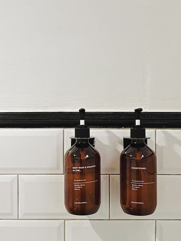 Two brown bottles of body wash and shampoo, and conditioner, hanging from a black bar against a white tiled wall.