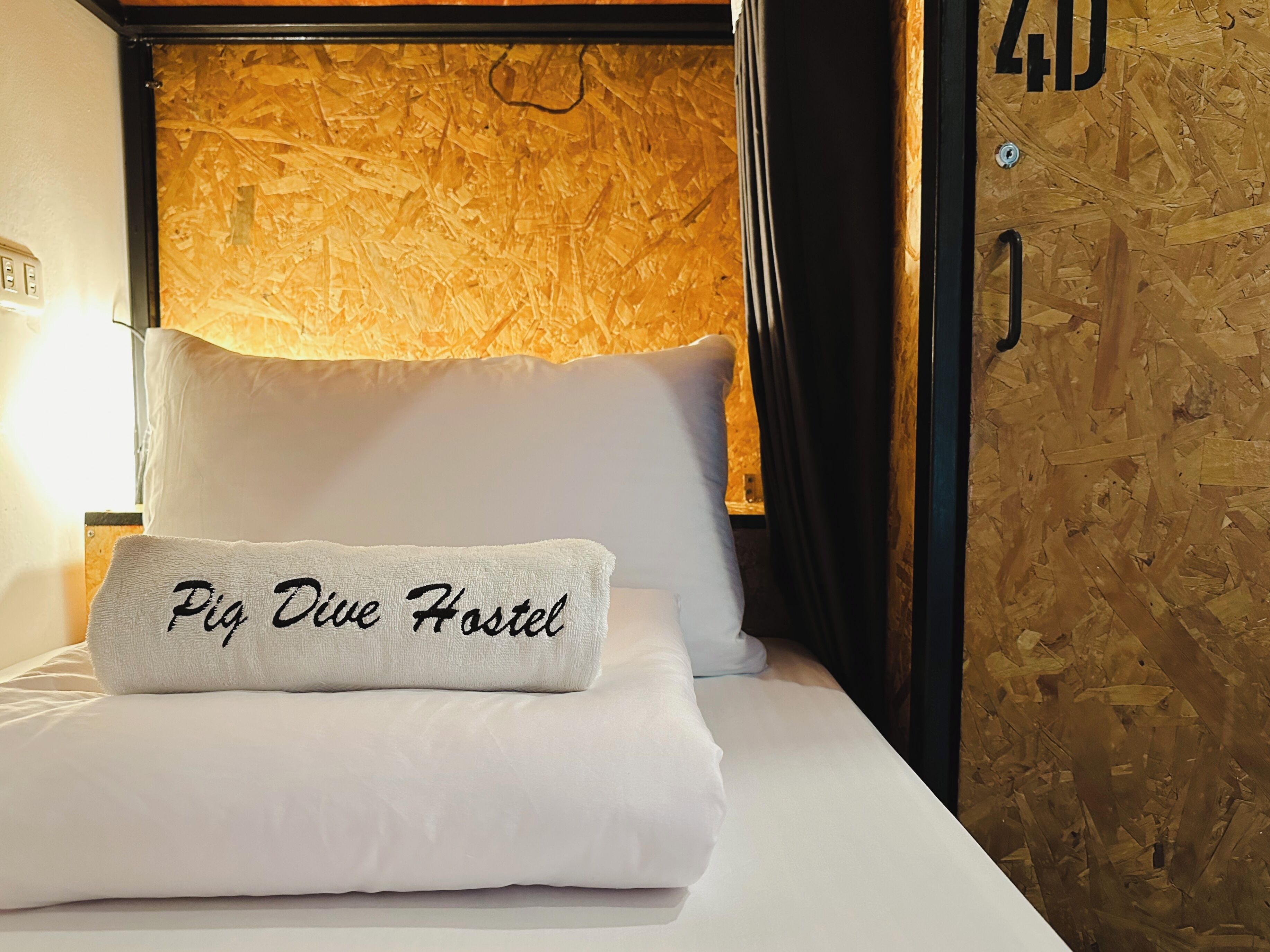 Una cama con un cojín que dice 'Pia Dive Hostel' y una pared de madera con textura.