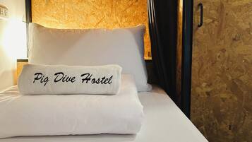 Una cama con un cojín que dice 'Pia Dive Hostel' y una pared de madera con textura.