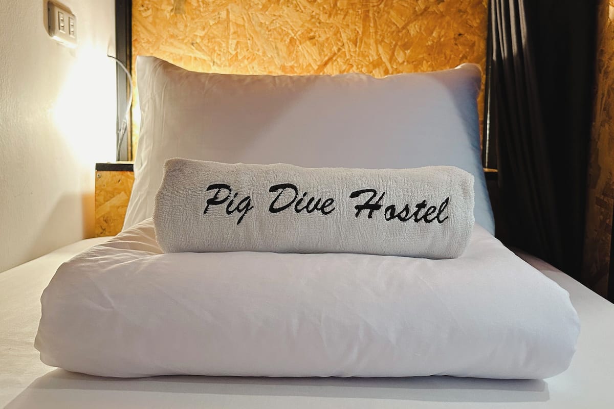 A bed with a pillow labeled 'Pig Dive Hostel' and a textured headboard.