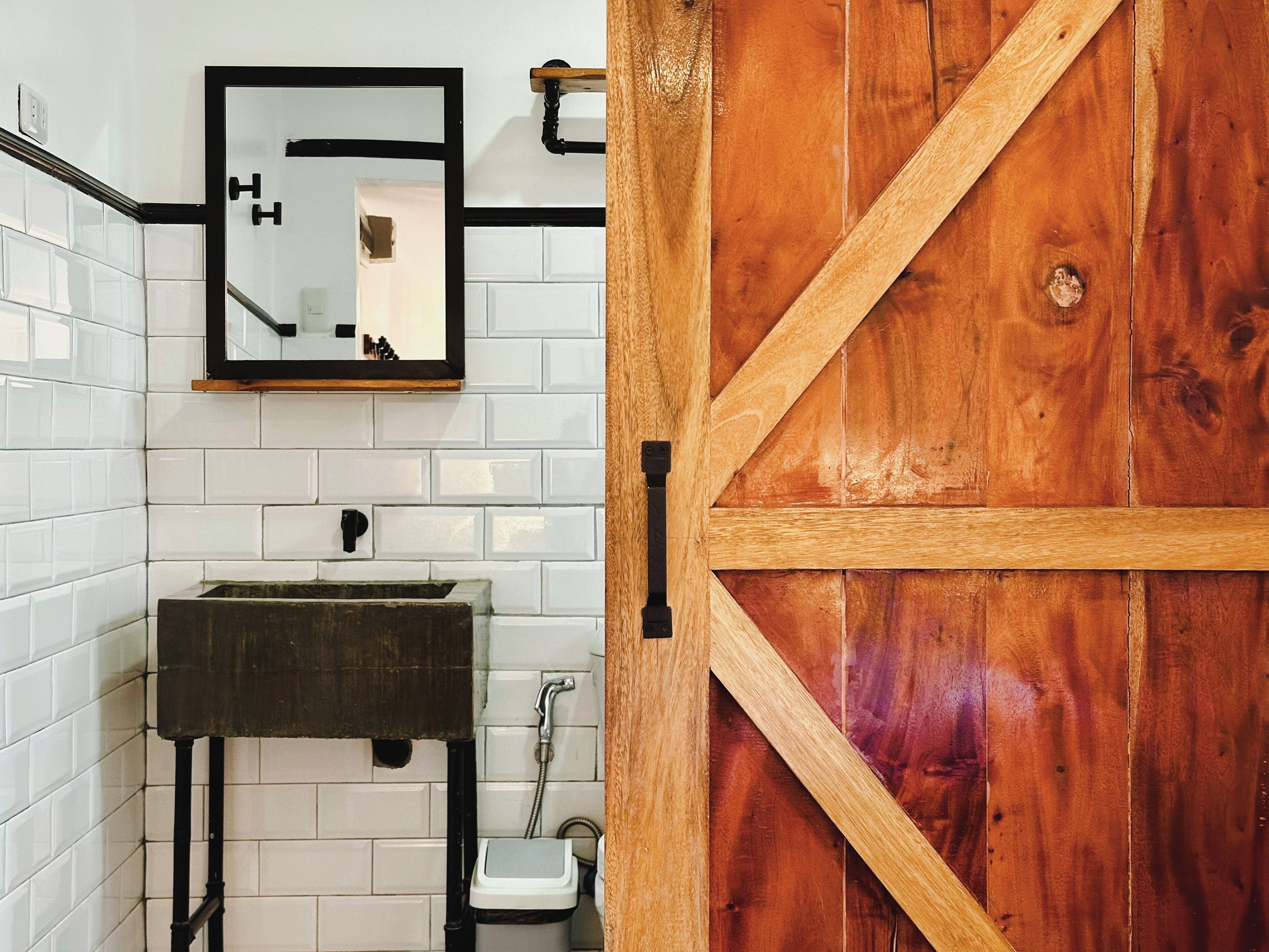 A bathroom with white tiled walls, a wooden door, a sink, and a mirror.