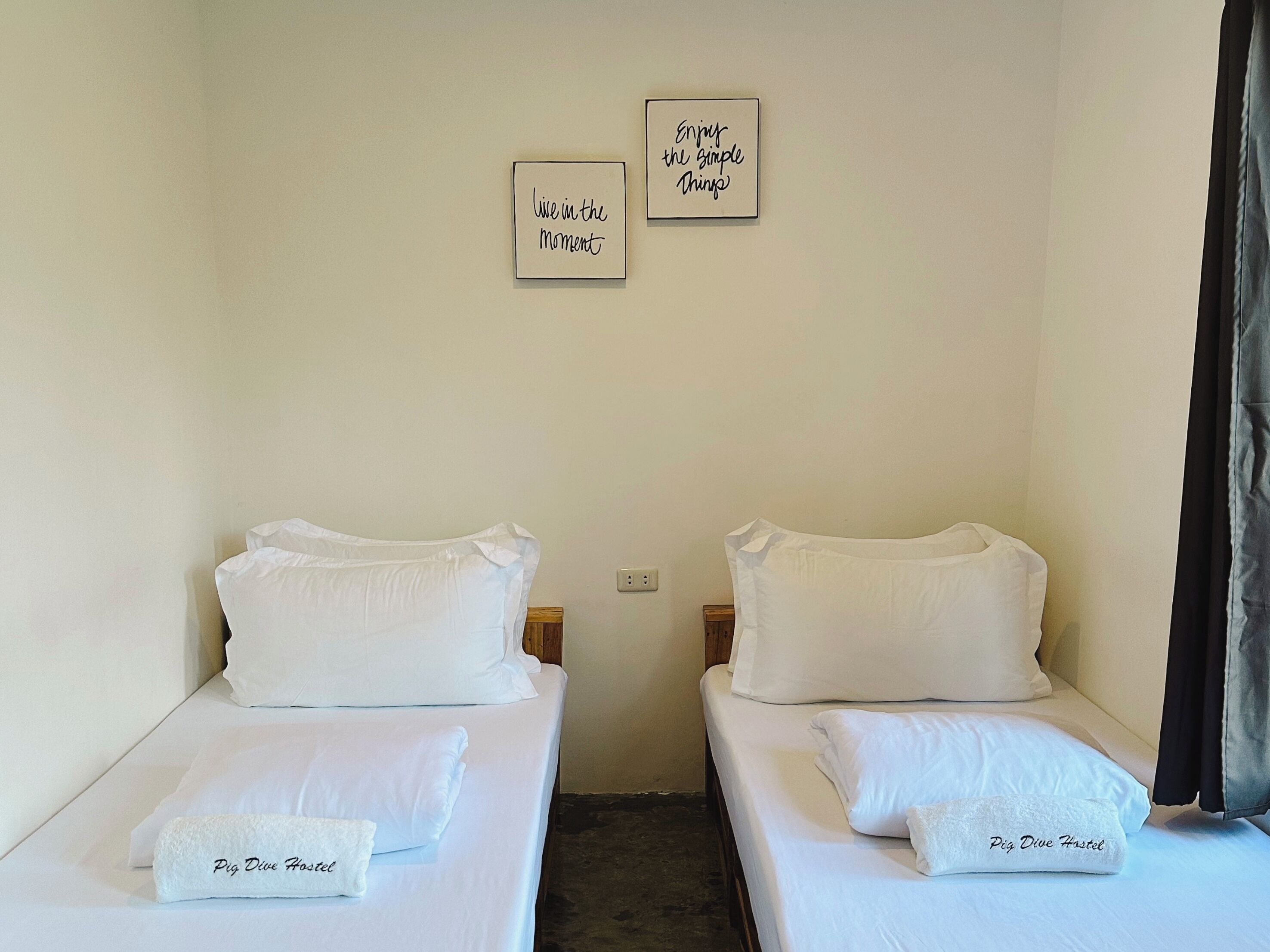 A hotel room with two single beds, each with a pillow and a towel labeled "Pig Dive Hostel". There are two motivational posters on the wall.