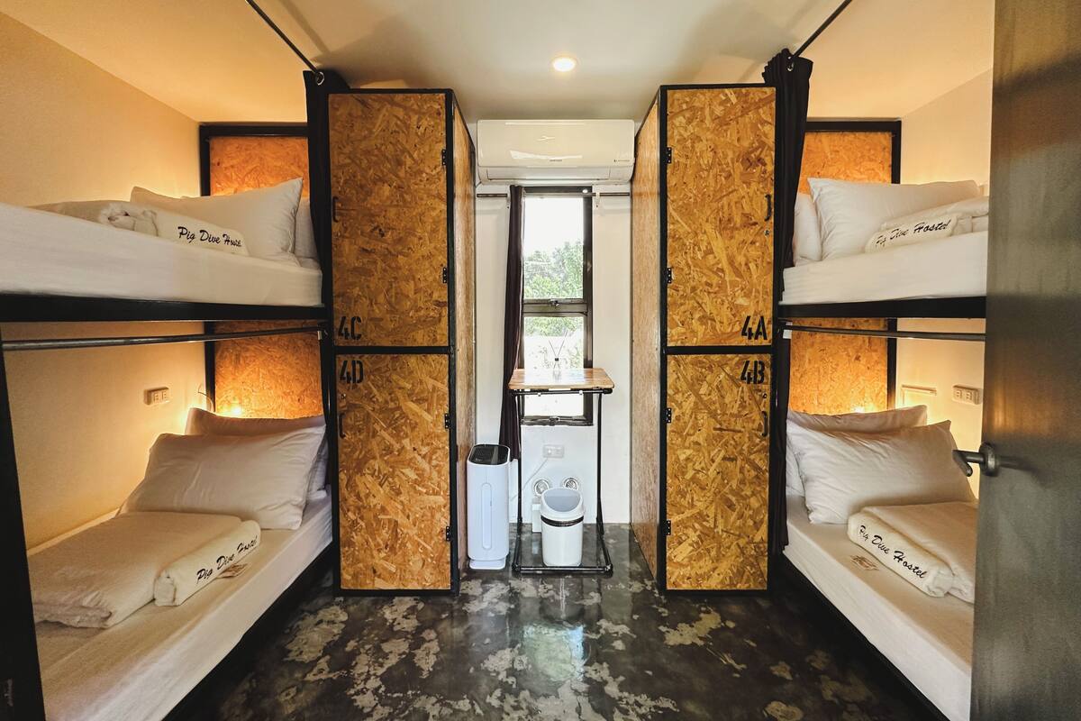 A hostel room with bunk beds, a small sink, and a window.