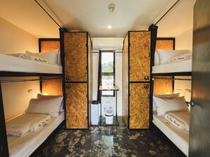 A hostel room with bunk beds, a small sink, and a window.
