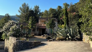 A Mediterranean-style villa with a stone wall, a patio with a table and chairs, and a large agave plant.