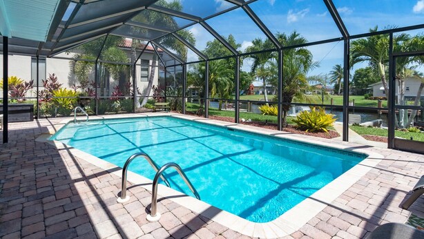 A covered outdoor swimming pool with a clear view of the surrounding landscape, including palm trees and a distant building. - Private All Inclusive Vacation Home Near Yacht Club and Ft Myers Beaches (Cape Coral)