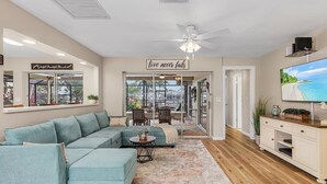 A living room with a sectional sofa, a coffee table, a TV, and a ceiling fan. - Private All Inclusive Vacation Home Near Yacht Club and Ft Myers Beaches (Cape Coral)