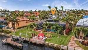 A residential area with a dock, a swimming pool, and a red umbrella. - Private All Inclusive Vacation Home Near Yacht Club and Ft Myers Beaches (Cape Coral)