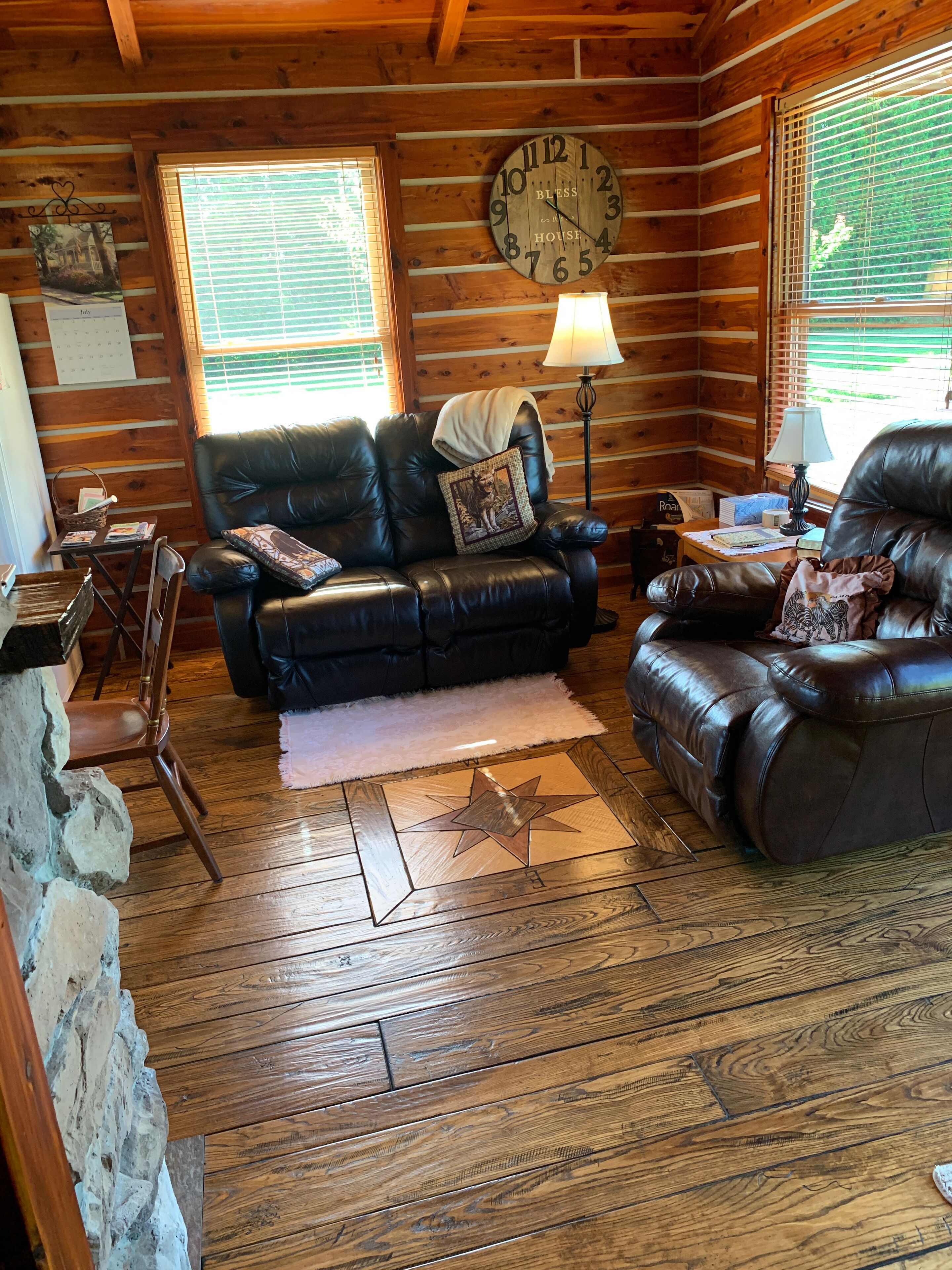 A cozy log cabin interior with a leather sofa, a wooden star-patterned rug, and a wall clock.