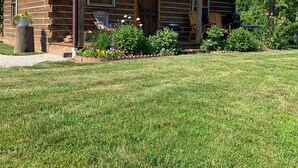 A rustic log cabin with a covered porch, a large window, and a well-maintained lawn.