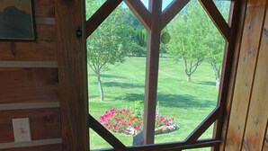 A wooden door with a geometric glass design, leading to an outdoor deck with a grassy lawn and a flower bed.