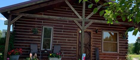 A rustic log cabin with a porch, outdoor seating, and a garden with colorful flowers.