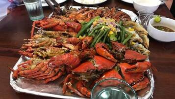 Una bandeja grande de mariscos cocidos, incluyendo cangrejos y pescado, acompañada de judías verdes y un recipiente pequeño con salsa.