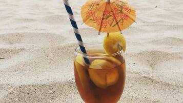 A cocktail glass with a straw and an umbrella on a sandy beach with a view of the ocean and hills in the background.