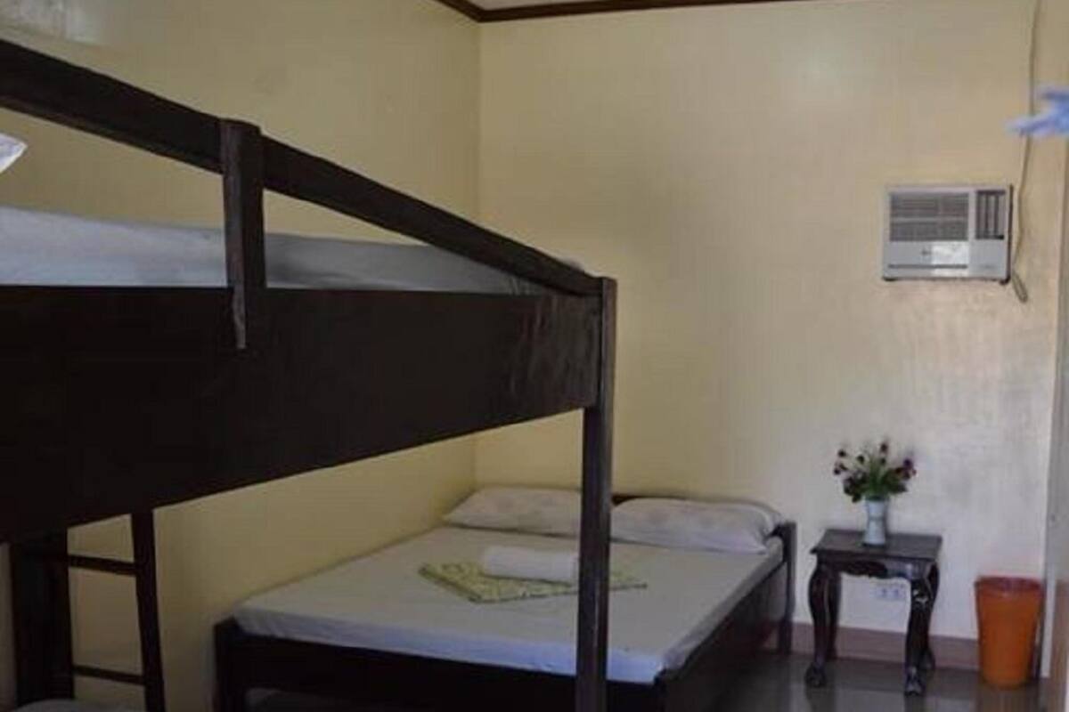 Une chambre avec deux lits superposés, une petite table de chevet ornée d’un vase et un appareil de climatisation fixé au mur.