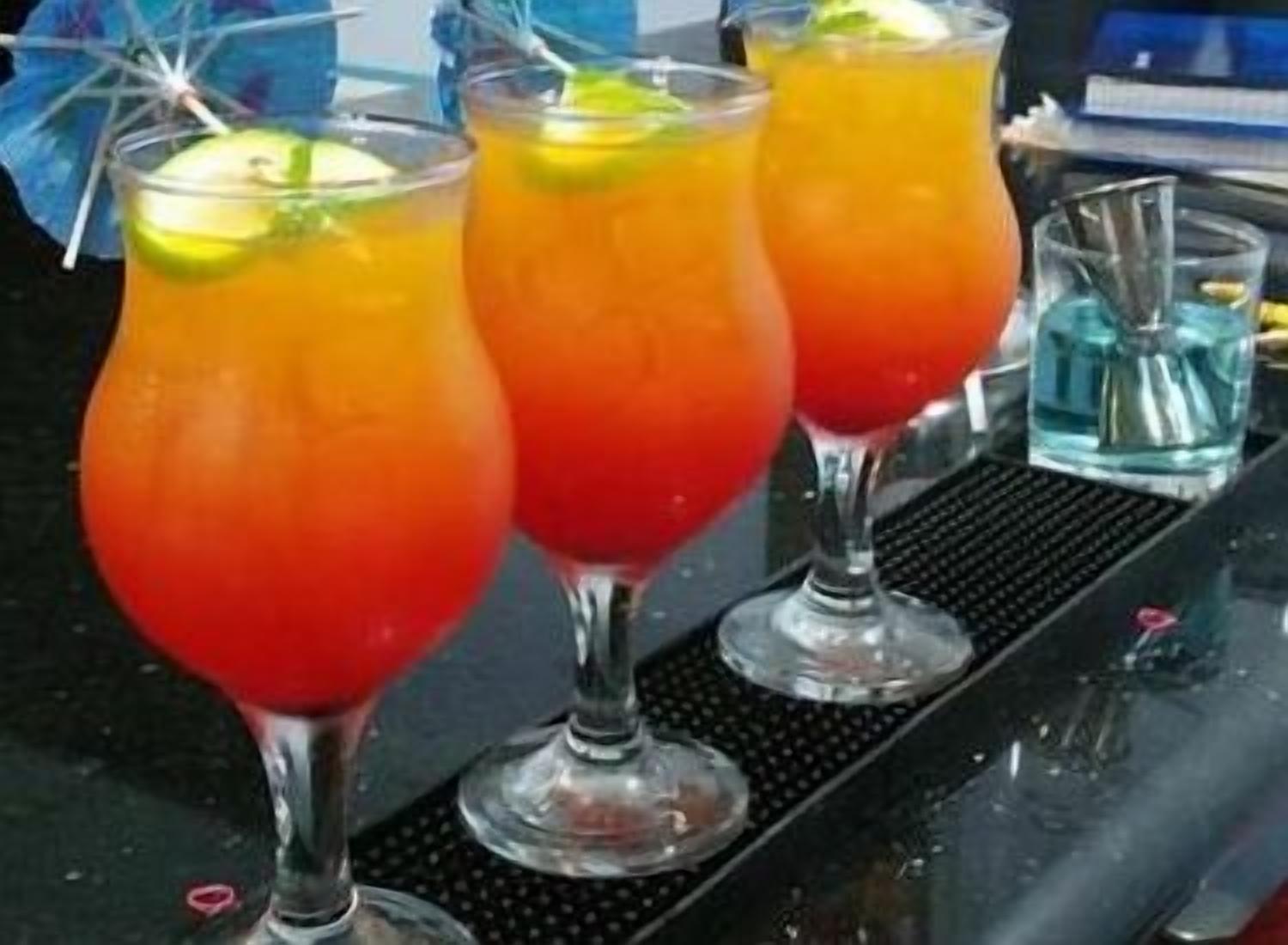 Trois grands verres contenant une boisson rouge-orangée, décorés de rondelles de citron vert, sont posés sur le comptoir d’un bar.