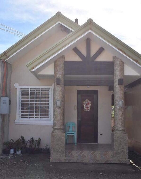 Una casa con porche delantero, una puerta adornada con un arreglo floral y una ventana con reja de metal.