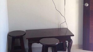 Een kamer met een flatscreen televisie aan de muur, een houten tafel met twee krukken en een deur aan de rechterkant.