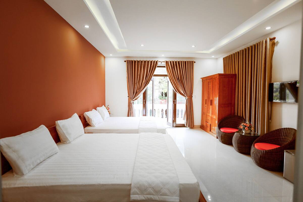 A hotel room with two beds, a wooden wardrobe, a TV, and a seating area with wicker chairs.