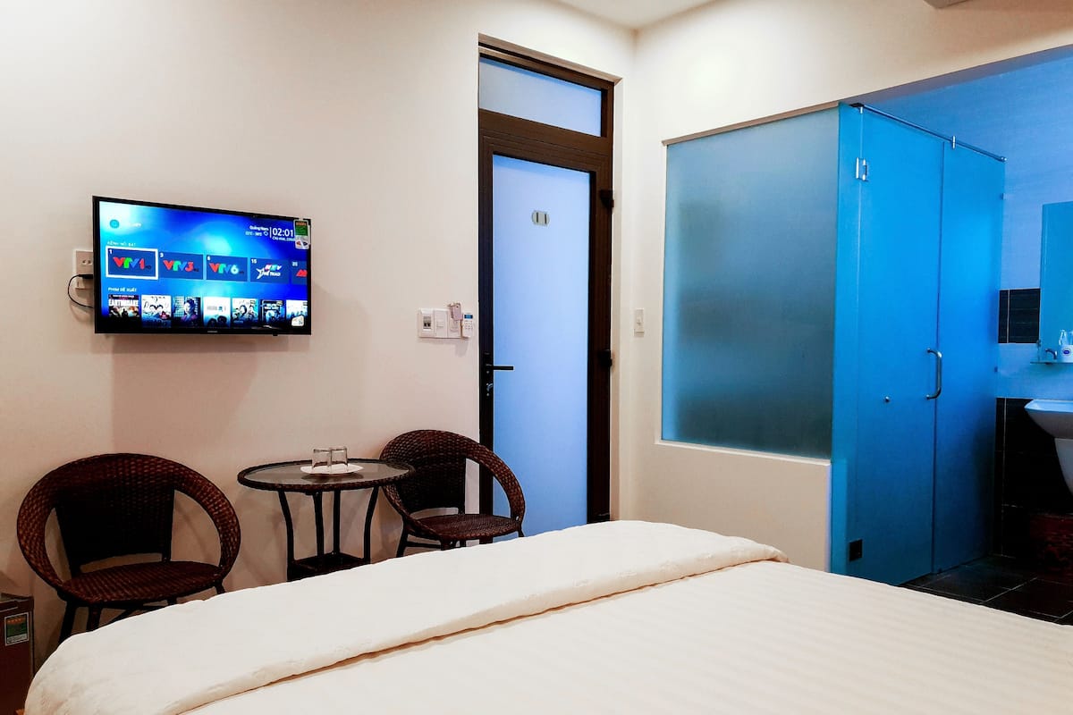 A hotel room with a bed, two chairs, a TV displaying a movie, a wardrobe, and a bathroom.
