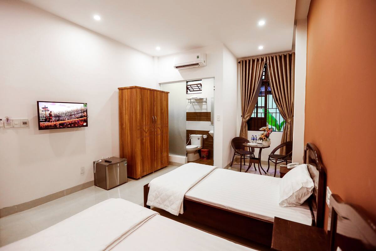A hotel room with two beds, a TV, a wardrobe, a bathroom, and a dining area.