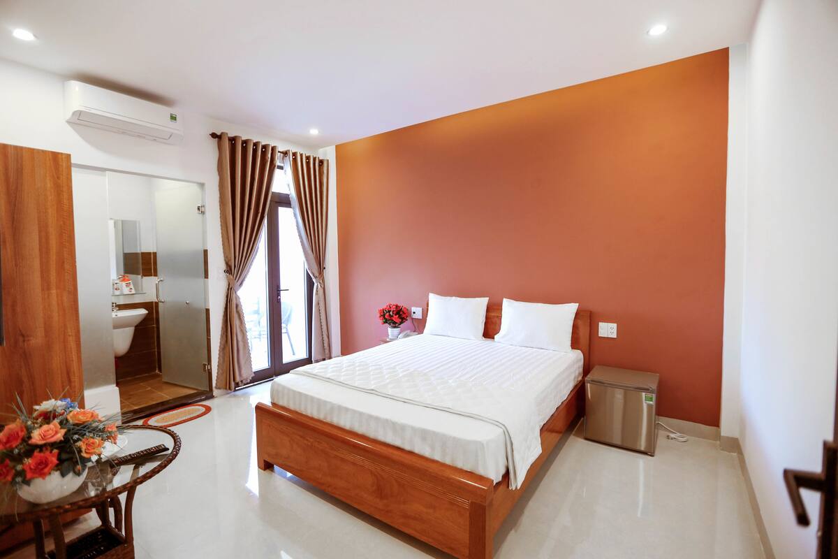 A modern hotel room with a large bed, a small bedside table, a mirror, and a view of the bathroom.