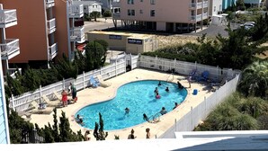 Edificio residencial con piscina rodeada por una cerca blanca, múltiples balcones y una vista despejada del mar.