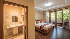 Quarto de hotel com cama de madeira, banheiro com pia e espelho, e varanda com vista para o verde.