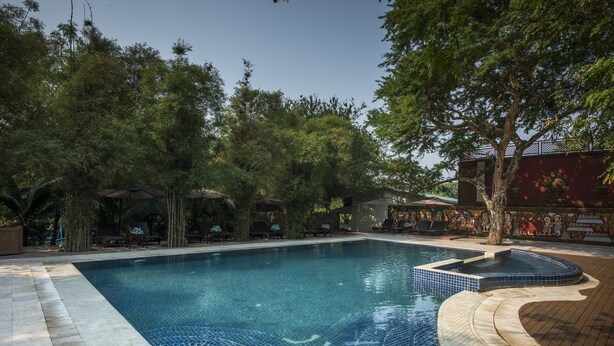 Uma piscina com borda em azulejo, cercada por árvores e um deck de madeira.