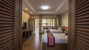 Quarto de hotel com duas camas, televisão e varanda com cortinas.