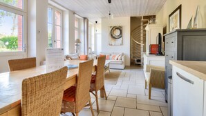 Amplia sala de estar con mesa de comedor, sillas de mimbre, sofá y una zona de cocina con refrigerador y armarios.