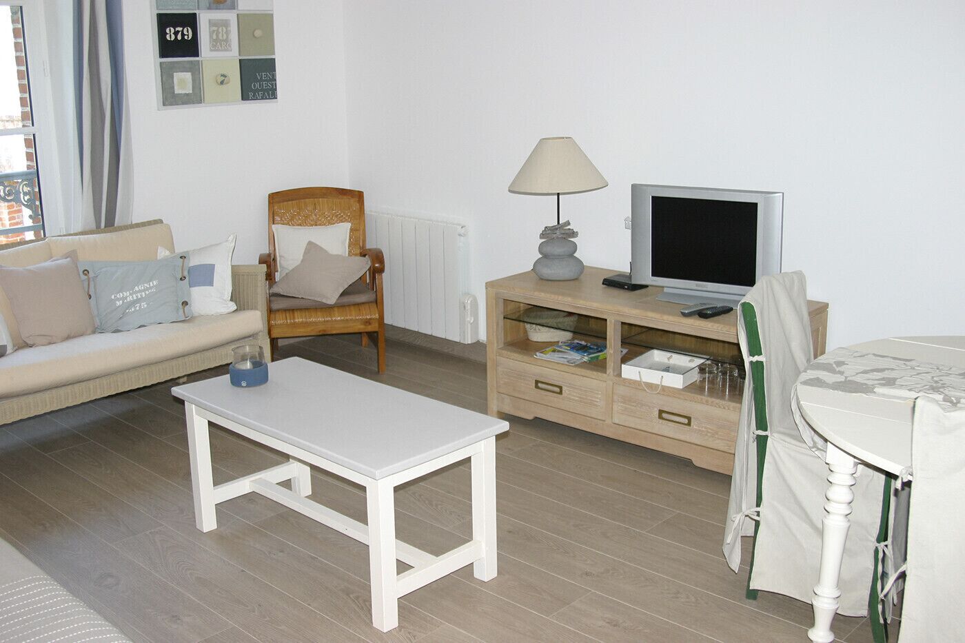 Una sala de estar con un sofá, una silla de madera, una mesa blanca, un mueble para televisión y una lámpara.