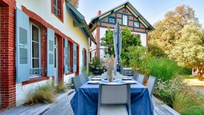 Un área de comedor al aire libre con una mesa dispuesta para cuatro personas, rodeada de sillas sobre una terraza de madera.