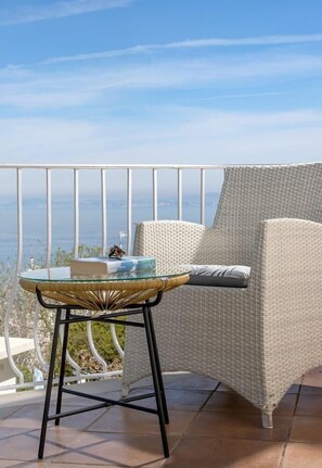 Un balcone con una sedia in vimini, un tavolino in vetro e vista sul mare.