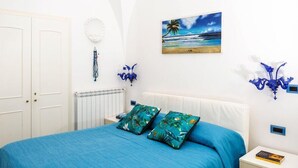 A bedroom with a bed, a painting of a beach, a wall-mounted lamp, and a decorative shell. - Il Sogno (Anacapri)