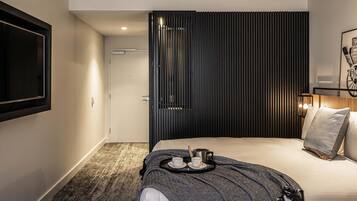 A modern hotel room with a bed, a tray with cups and a kettle, a framed picture on the wall, and a door with a vertical panel design.
