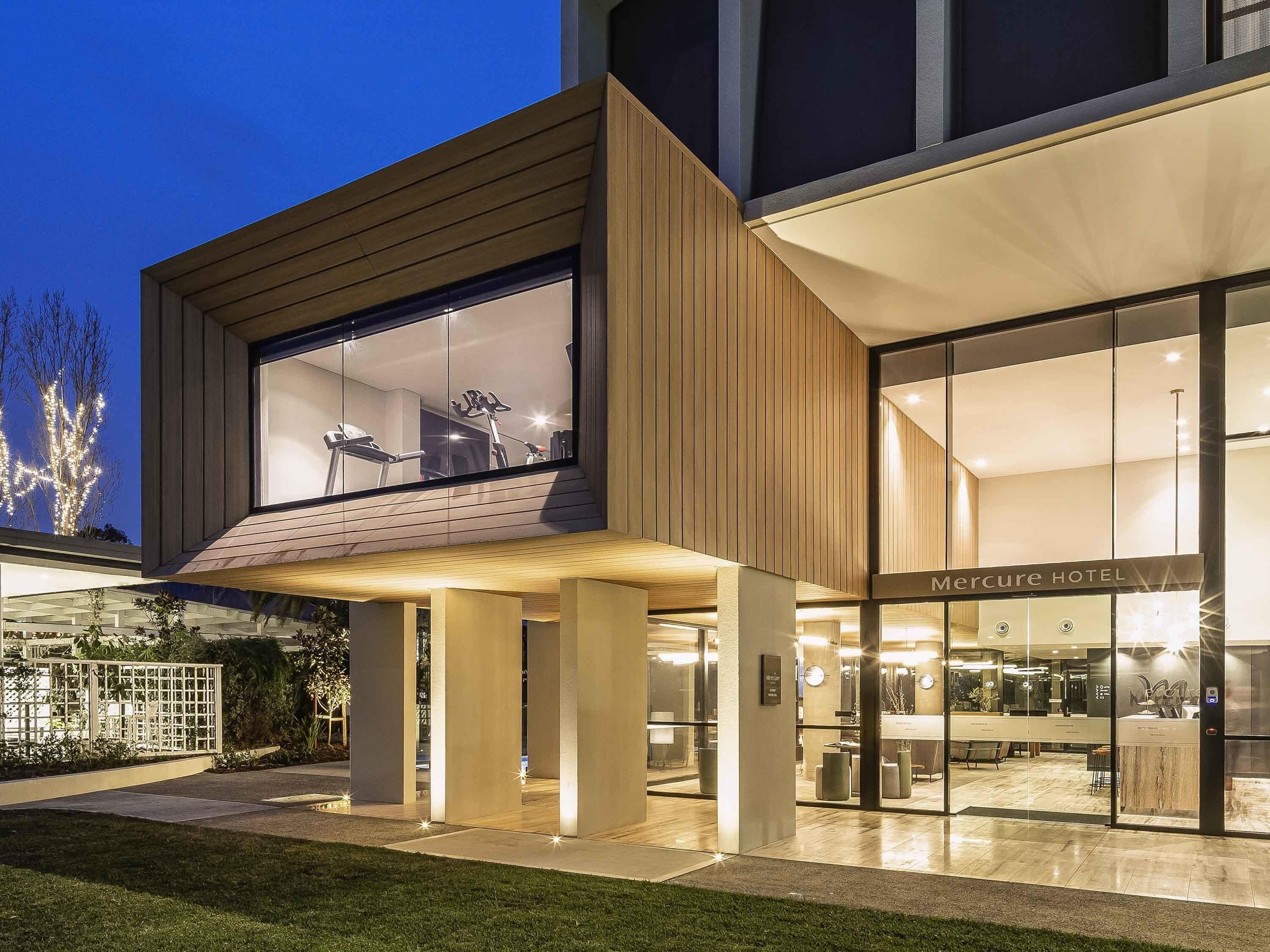 A modern hotel with a glass facade, outdoor seating area, and a visible elevator.