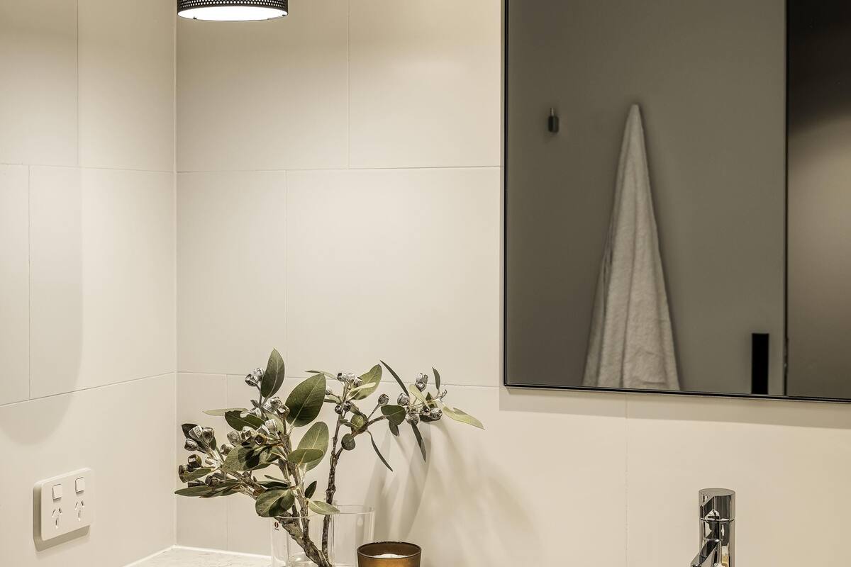 A bathroom with a white tiled wall, a mirror, a sink with a faucet, a plant, and a candle.