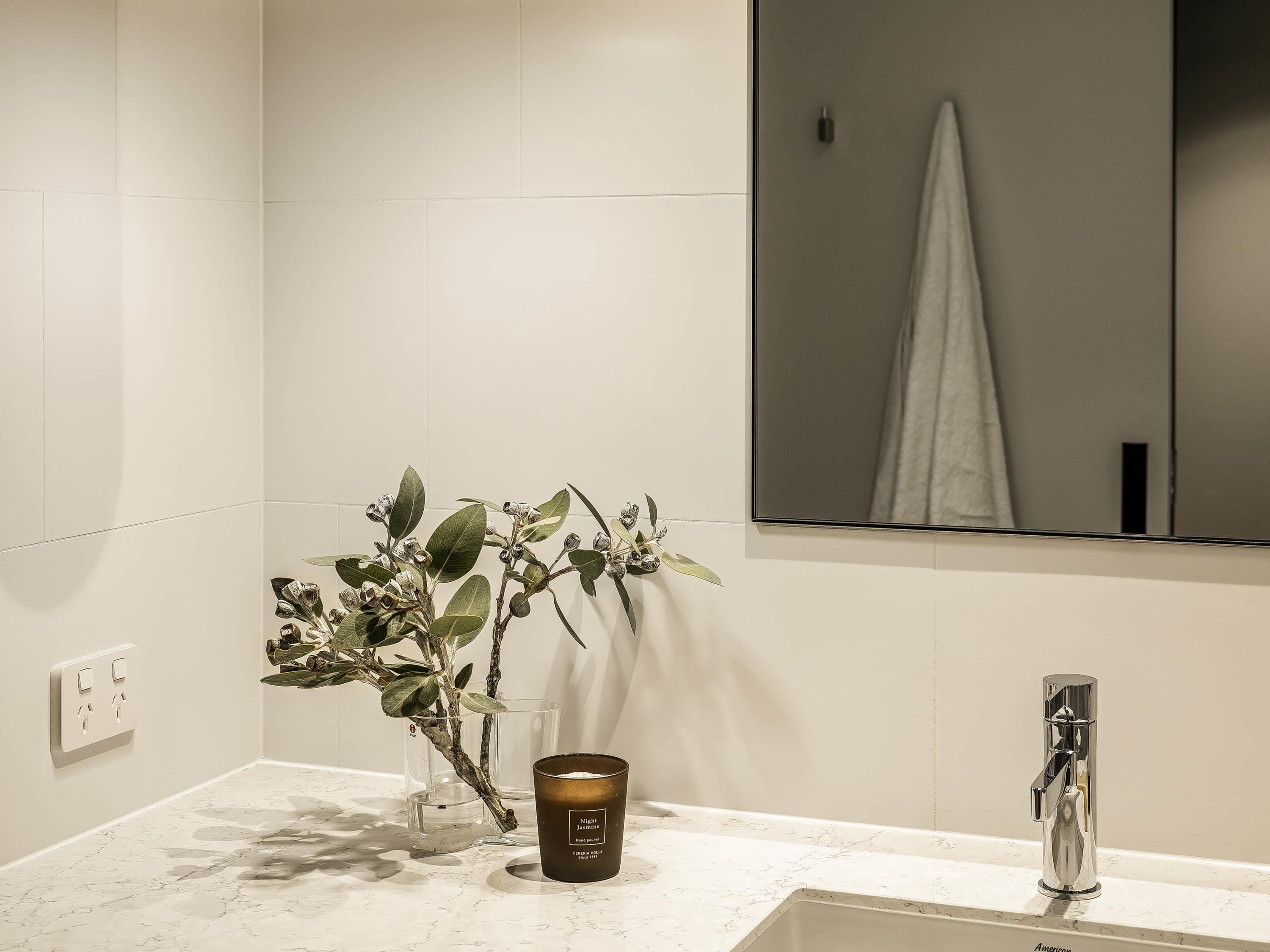 Un baño con pared de azulejos blancos, un espejo, un lavabo, un grifo y una vela.