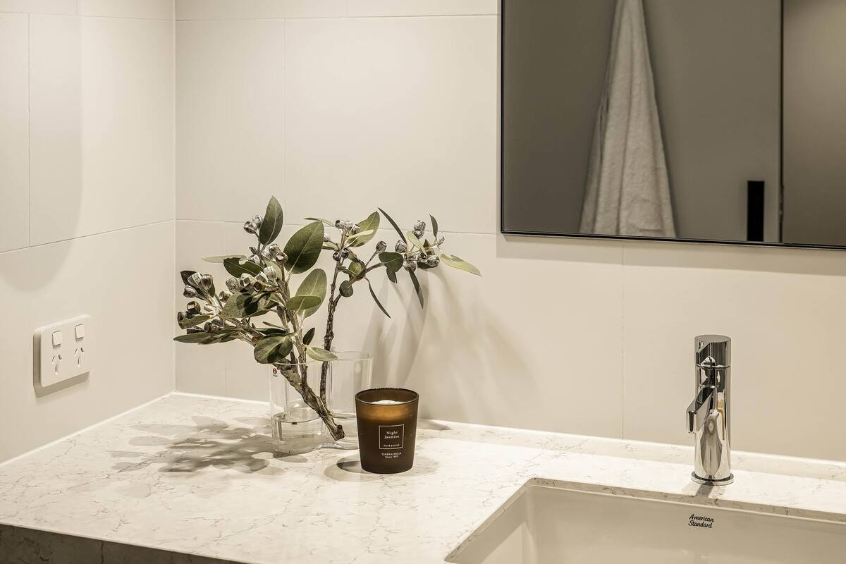 A bathroom with a white marble countertop, a hand soap dispenser, a candle, and a mirror with a towel hanging.