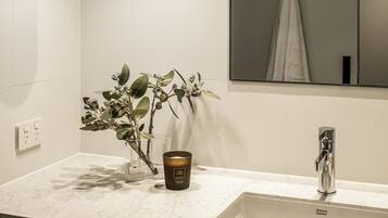 Une salle de bain avec un mur recouvert de carreaux blancs, un lavabo avec un robinet chromé, un porte-bougie en verre et une plante en pot.