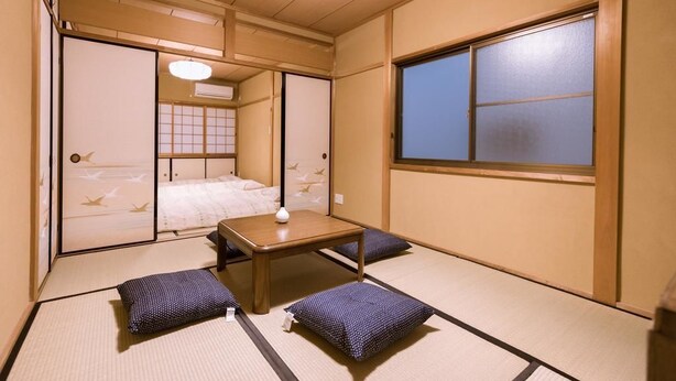 Una habitación tradicional japonesa con suelo de tatami, una mesa de madera baja y una cama con ropa de cama blanca.