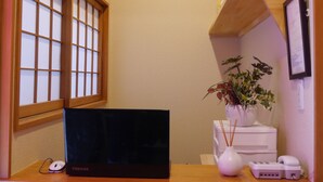 Un pequeño espacio de oficina con un escritorio, una computadora portátil, un jarrón con flores, un teléfono y una estantería con objetos decorativos.
