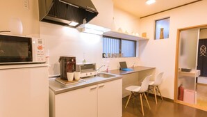 Cocina compacta con microondas, estufa y pileta. Se observa una ventana con persianas y una repisa con objetos decorativos.