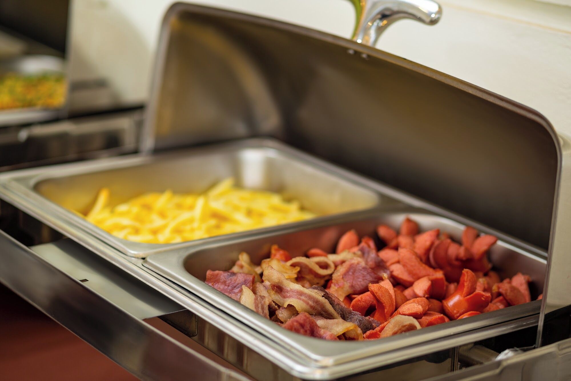 A buffet with trays of scrambled eggs, bacon, and French fries.