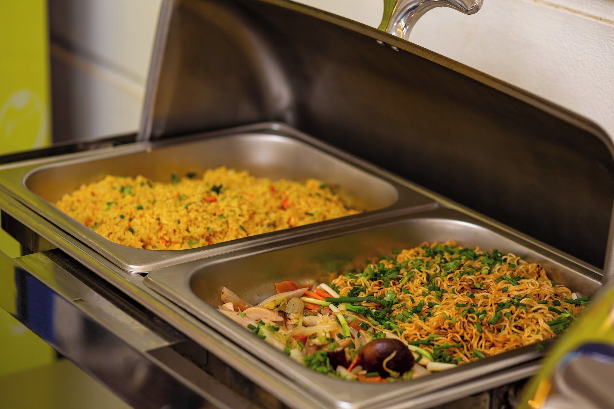 A buffet with two trays of food, one with yellow rice and the other with noodles and vegetables.