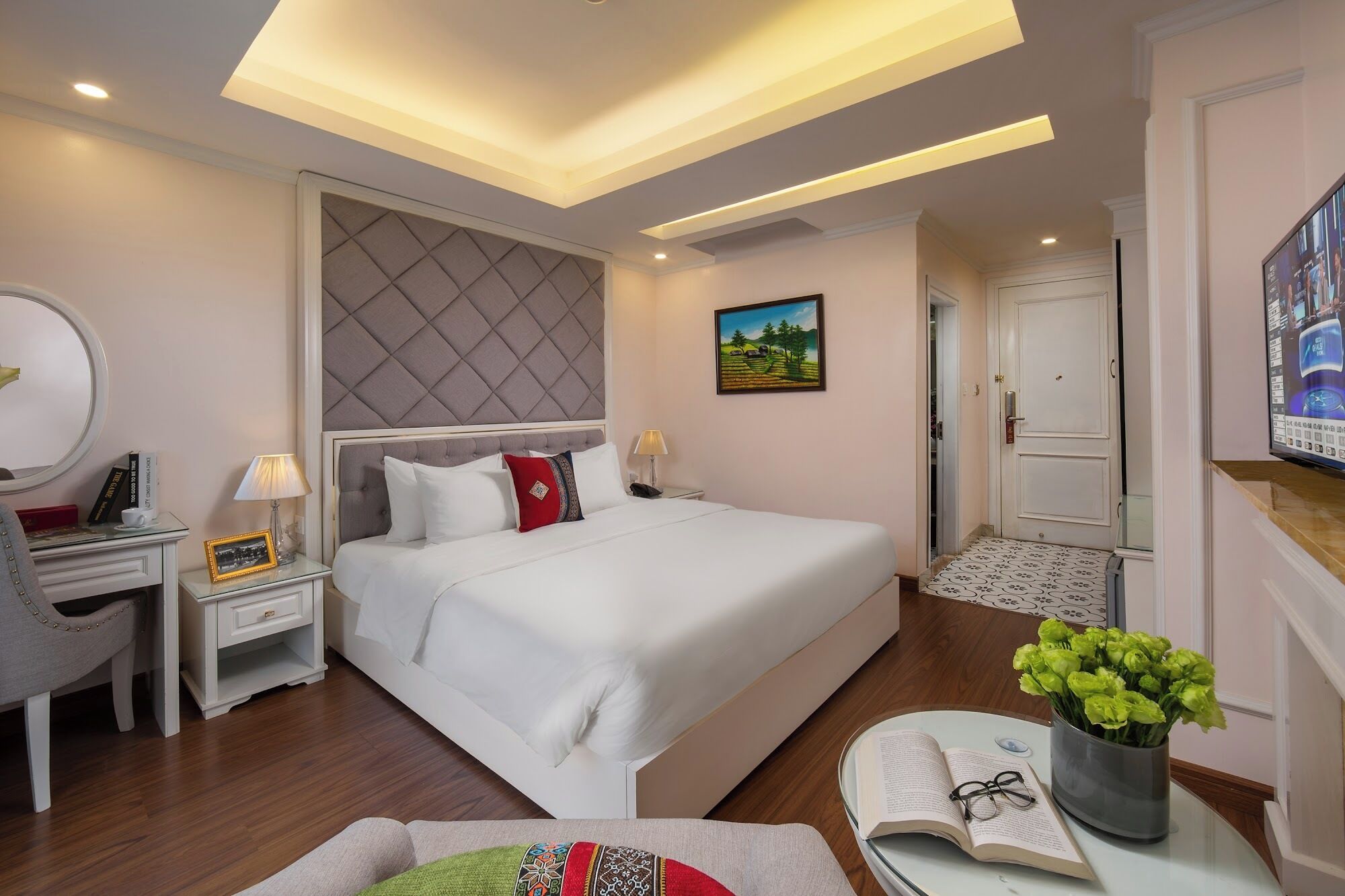 Une chambre d’hôtel avec un grand lit, des tables de chevet, un bureau, une chaise, un miroir, un tableau et un téléviseur.